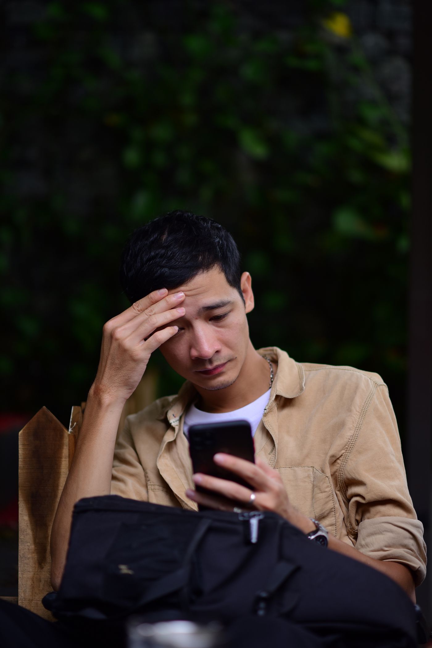 スマートフォンを見ながら考え込む男性